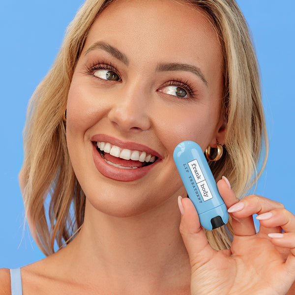 Woman applying a blue skincare product to her face against a blue background