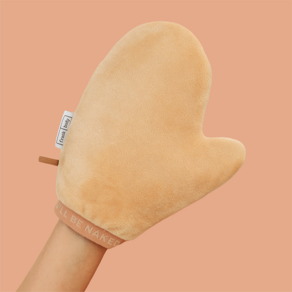 A hand wearing the frank body Double Trouble Tanning Mitt against a tan background.
