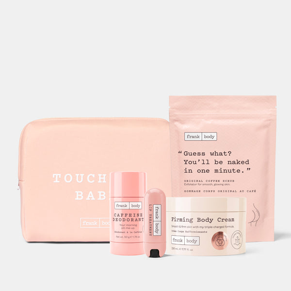 A Frank Body gift set featuring a blush pink zippered pouch, a deodorant stick, a body cream tube, and a body scrub packet, all arranged on a light gray background.