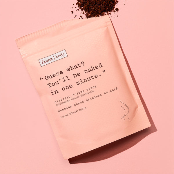 A pink stand-up pouch of Frank | Body Original Coffee Scrub styled on a matching pink background with coffee grounds scattered at the top.