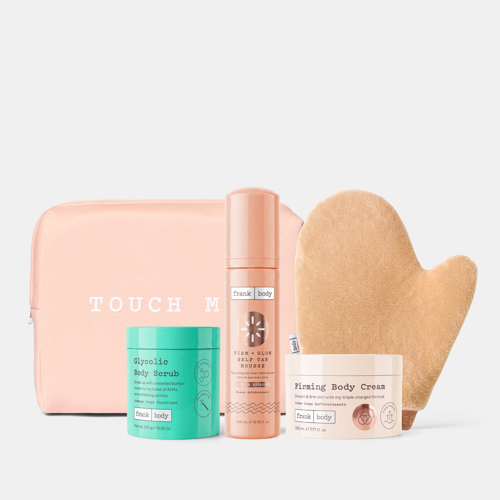 A Touch of Beauty self-care set featuring a blush pink zippered pouch with 'TOUCH OF BEAUTY' printed in white, a mint green Glycolic Body Scrub jar, a peach-colored Firming Glow Body Lotion bottle, a beige heart-shaped exfoliating mitt, and a cream-colored Firming Body Cream jar, all arranged on a light gray background.