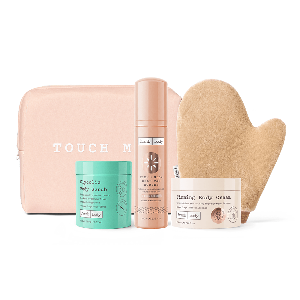 A Touch of Beauty self-care gift set featuring a blush pink zippered pouch, a mint green Glycolic Body Scrub jar, a peachy-pink Fizzy Glow Body Oil bottle, a white Fizzy Glow Body Cream jar, and a beige muslin body towel, all arranged on a clean white background.