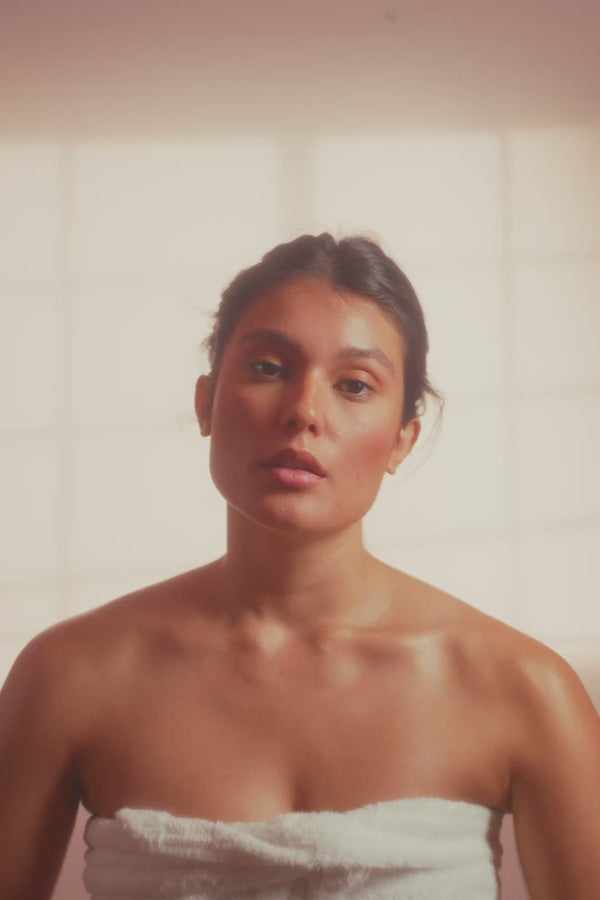 frank body Firm + Glow Tanning Jelly video: a woman wrapped in a towel in a sunlit room.
